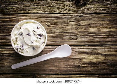 Tub of creamy Italian ice cream with a plastic disposable takeaway spoon served on an old weathered wooden table at a cafeteria for a refreshing summer treat, overhead view with copyspace