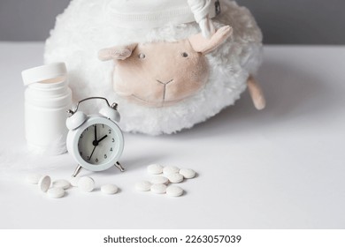 A tube of pills, a sheep in a sleep cap and an alarm clock. The time on the clock is 2 am. Insomnia and recovery of sleep mode. Count sheep to fall asleep.