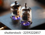 The tube sound, the valve sound. A vacuum tube in a socket of an audio device, with a glowing heater or filament. Shallow depth of field.
