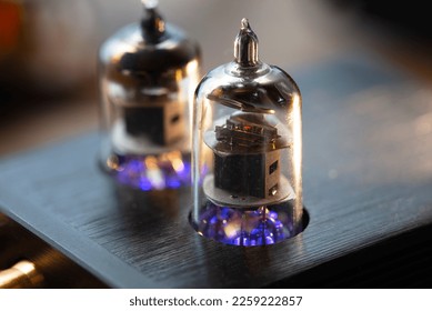 The tube sound, the valve sound. A vacuum tube in a socket of an audio device, with a glowing heater or filament. Shallow depth of field.
