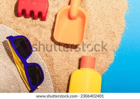 A tube of sunscreen, sunglasses and children's beach toys on the sand.