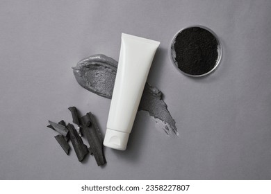 A tube without label is decorated with a smear of clay mask and a petri dish of activated charcoal powder. Activated bamboo charcoal can improve dry or oily skin, or heal acne - Φωτογραφία στοκ