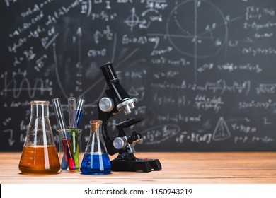 Tubes with chemical liquids stand on a wooden table on a chalkboard background with digital formulas