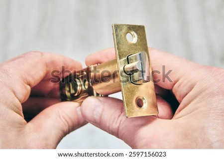 Tubular door latch with rectangular strike plate in human hands, close up.