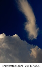 tuft of cloud shaped by the winds in a curious shape floating, above a white cloud, under a blue sky.