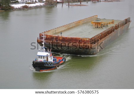 A tug boat hauls a large, empty barge down river/Tug Boat and Large Empty Barge/A tug boat hauls a large, empty barge down river. 