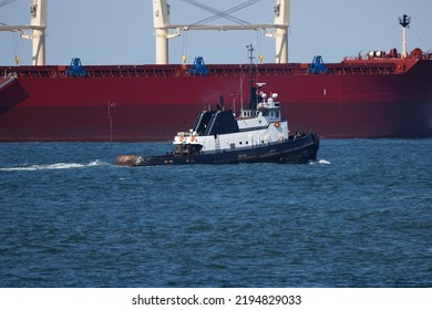 A Tug Boat Sailing In Front Of A Large Red Ship In The Coastal Waters Of Westport, Washington.