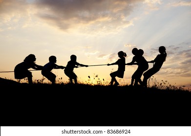 Tug war, pulling rope, children playing on meadow, sunset, summertime