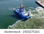 A tugboat in port stands ready alongside the ship waiting to provide support
