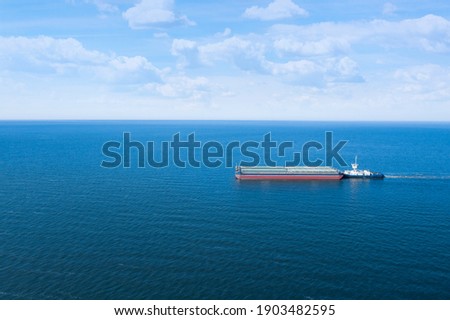 Tugboat pulling barge with cargo by water, aerial view