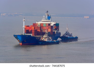 Tugboats help turn around a container vessel on the way out of the harbor. - Powered by Shutterstock