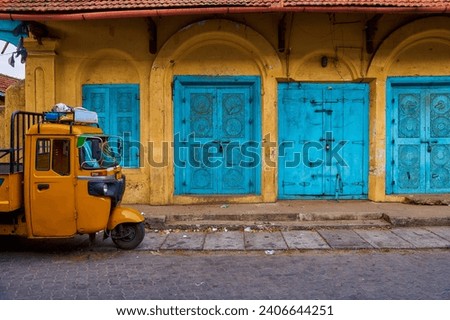 tuk tuk auto rickshaw standing against the background of an old colonial building with blue wooden doors - Indian street concept background                               
