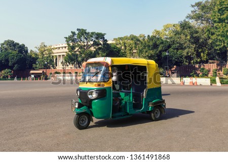 Tuk tuk - traditional indian moto rickshaw taxi on one of the street of New Delhi. yellow green tricycle stands on the square against the background of the presidential Palace. 
