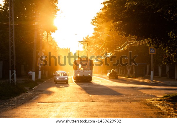 TULA, RUSSIA -\
JUNE 6, 2013: Car and tram on traffic light stop under golden sun\
backlight. Air glowing\
bright.
