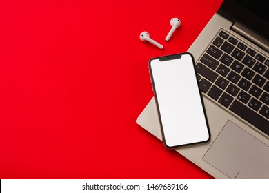 Tula, Russia - May 24,2019: Apple IPhone X And Airpods On Red Background With Notebook. The Screen Of The Smartphone Is White. Mockup.