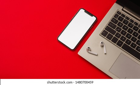 Tula, Russia - May 24,2019: Apple IPhone X And Airpods On Red Background With Notebook. The Screen Of The Smartphone Is White. Mockup.