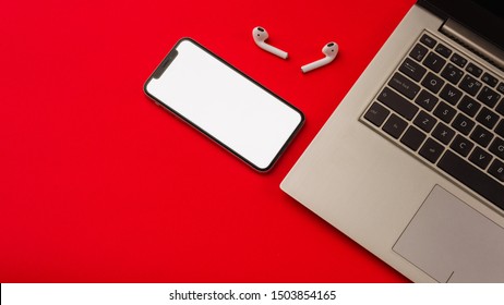 Tula, Russia - May 24,2019: Apple IPhone X And Airpods On Red Background With Notebook. The Screen Of The Smartphone Is White. Mockup.