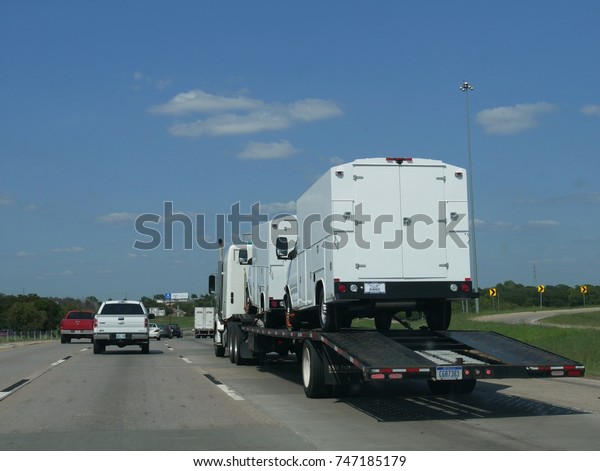 TULSA, OKLAHOMA—JUNE 2017: A trailer truck transporting\
two white cargo trucks join the traffic along the road to Tulsa,\
Oklahoma. 