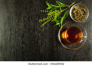 Tulsi or holy basil tea in transparent glass cup with fresh tulsi leaf and dried leaf in wooden bowl on black wooden background top view. Ayurvedic medicine in India. - Powered by Shutterstock