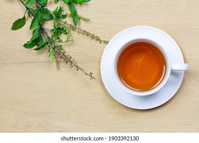 Tulsi Or Holy Basil Tea In White Cup With Fresh Tulsi Branch On Wooden Background Top View. Ayurvedic Medicine In India.