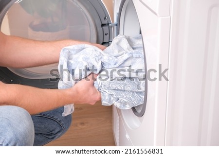 tumble dryer. A man takes dried bed linen out of the tumble dryer. Dryer machine in the house.