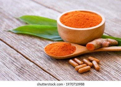 Tumeric powder capsules, Turmeric root ( curcumin, Curcuma ) with green leaf isolated on wood table background.  - Powered by Shutterstock
