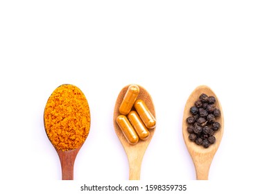 Tumeric powder, Curcumin capsule and black peppercorn in wooden spoon  isolated on white background.  Natural herbal medical plant concept. Top view. Flat lay.