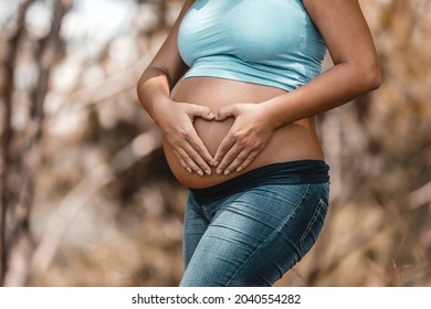 Tummy of a Pregnant Woman. Making Heart Shape by her Hands on Belly. Body Part. Enjoying Pregnancy. Young Happy Family.