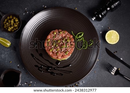 Tuna and avocado tartare with sesame seeds and capers on a dark ceramic plate
