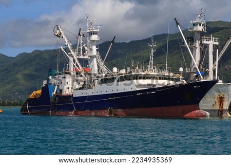  tuna boat are moored to a cargo ship in the harbor.