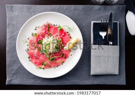 tuna carpaccio served on white plate. Close up Raw tuna tenderloin with copy space. Fresh italian appetizer. Seafood italian mediterranean cuisine