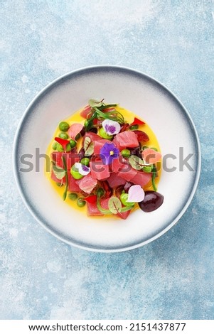 Tuna ceviche with cherry and wakame seaweed decorated with flowers over light blue background. Overhead view, copy space