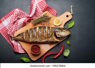 Tuna (fish)  baked with spices and lemon on a wooden cutting board. Near herbs and spices such as thyme, basil and pink pepper. Dietary Mediterranean cuisine.