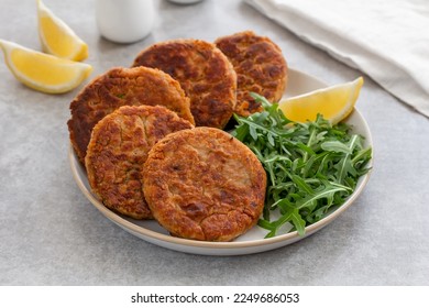 Tuna Patties or small fish cakes made with canned tuna, white beans, herbs and potato served on a plate with arugula salad and lemon wedges. Selective focus, gray concrete background. Horizontal. - Powered by Shutterstock