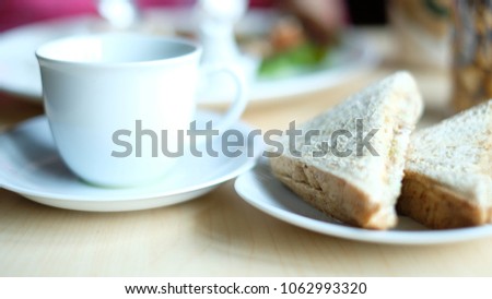 Tuna sandwiches on a white plate are beside tea cup