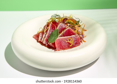 Tuna Tataki In Sesame With Salad. Fish Sashimi Restaurant Appetizer On White Table With Green Wall. Day Sunlight With Hard Shadow Of Tropical Palm Leaves. Summer Or Spring Food Concept