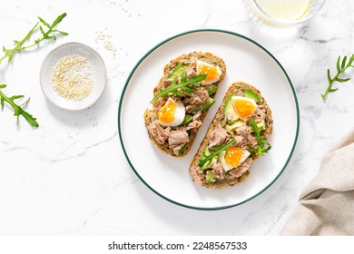 Tuna toast. Open sandwiches with whole grain bread, canned tuna, boiled egg, avocado and arugula. Top view - Powered by Shutterstock