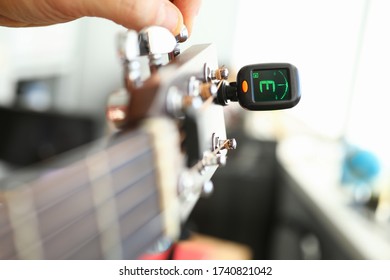 Tuner is installed on guitar neck for tuning notes. Tuner for an acoustic guitar. Each string makes reference sound. Musician guitar workshop. Specialist will assist in improving tool - Shutterstock ID 1740821042