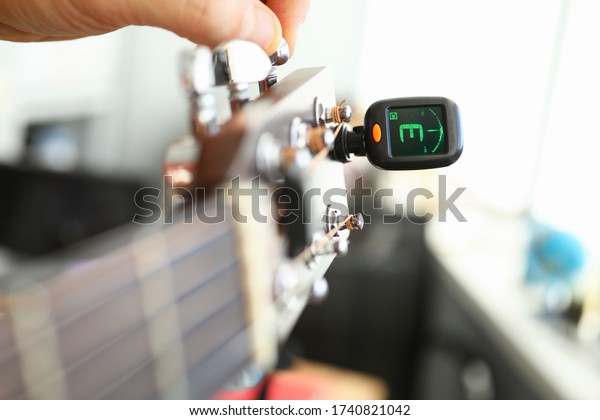 Tuner\
is installed on guitar neck for tuning notes. Tuner for an acoustic\
guitar. Each string makes reference sound. Musician guitar\
workshop. Specialist will assist in improving\
tool