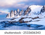 Tungeneset or Devils Jaw mountain on Senja island, Norway in winter. Winter landscape with snowy mountain peaks, fjord waters and ice coast in northern Norway. Scenic view with dramatic sky.