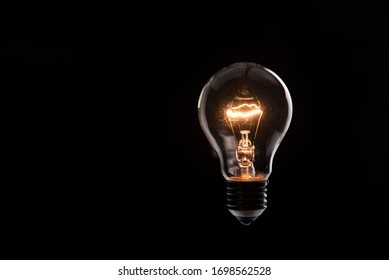 tungsten light bulb lit on black background - Powered by Shutterstock