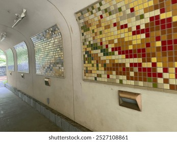 A tunnel with curved walls features vibrant mosaic tile panels in shades of yellow, red, and green. The geometric patterns add a touch of color to the otherwise plain, light-colored interior of the tu - Powered by Shutterstock