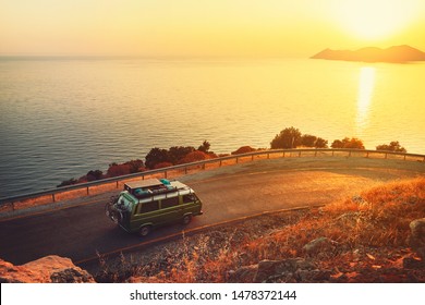 Turkey, Antalya - JULY 10, 2019: Old Timer Classic Camper Van Cruising Down The Curvy Road Following The Seacoast With The Beautiful Sunset Over Hills And The Sea. Road Trip Background.