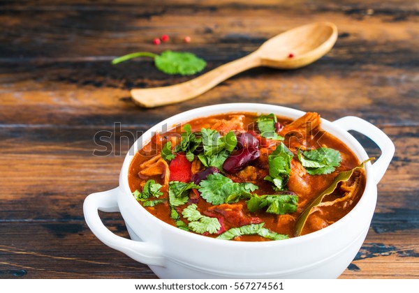 Turkey Chili. Stewed with black and\
white beans, tomatoes, bell pepper, onion, garlic, thyme, cinnamon,\
chocolate and fresh cilantro. Soup bowl on wooden\
table.