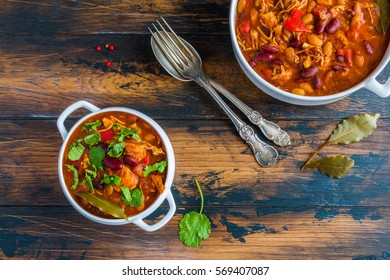 Turkey chili in white bowl and casserole on wooden table, top view. 
