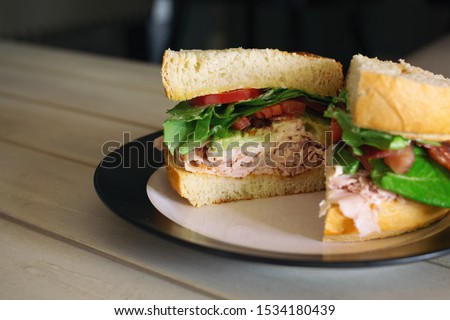 Turkey club sandwich with avocado, bacon and tomato on fresh bread cut in half. 