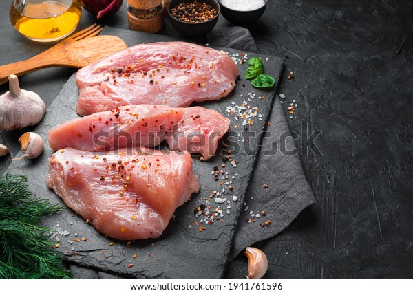 Turkey fillet with spices,\
dill and garlic on a black background. Top view, culinary\
background.