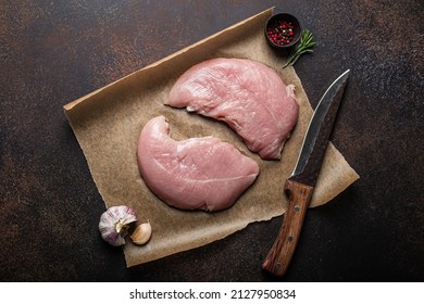 Turkey Lean Raw Fillet On Baking Paper With Rosemary, Garlic And Spices On Dark Brown Rustic Concrete Background With Knife From Above Flat Lay, Healthy Diet Turkey Meat Ready To Be Cooked