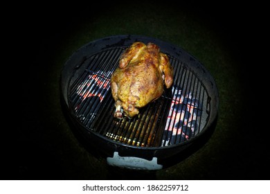 Turkey on a charcoal grill, indirect cooking, in the dark, copy space. Traditional grilled, turkey, slow cooked smoked flavor. Surrounded by black negative space and glowing coals. on a kettle grill.