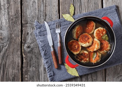 turkey potato cakes browned and boiled in red pot on rustic wooden table with bay leaves and cutlery, horizontal view from above, flat lay, free space - Powered by Shutterstock